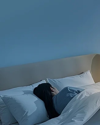 침대에 누워 있는 사람이 하얀 베개와 이불을 덮고 잠들어 있는 모습입니다. 벽은 부드러운 파란색으로 칠해져 있으며, 방 안은 차분하고 조용한 분위기를 자아내고 있습니다.