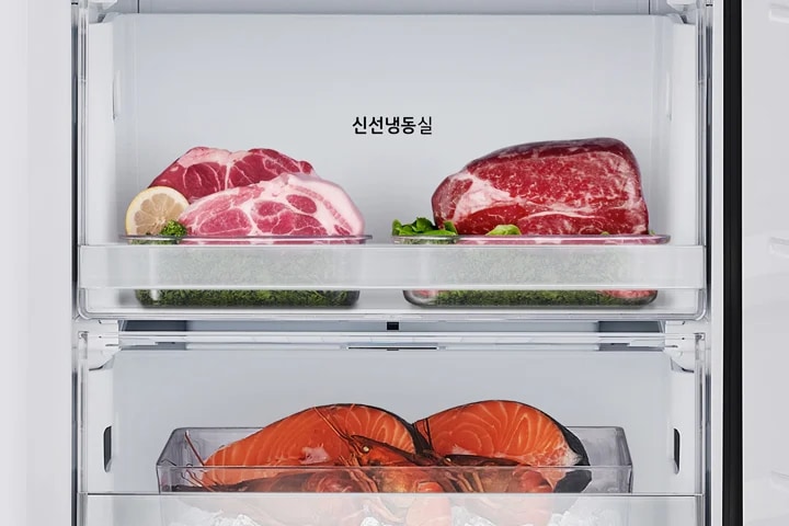 냉장고 내부에 두 개의 투명한 서랍이 보이며, 위쪽 서랍에는 신선냉동실이라는 텍스트가 있습니다. 서랍 안에는 레몬 조각과 함께 돼지고기와 소고기가 각각 놓여 있습니다. 아래쪽 서랍에는 얼음 위에 연어와 바닷가재가 담겨 있습니다.